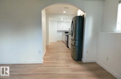 Archway entry leading to kitchen with wood-finish flooring, recessed lighting, stainless steel appliances, and white cabinetry - 183 Dechene Road, Edmonton, AB 