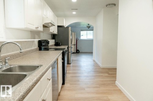 Kitchen featuring white cabinetry, a double basin stainless steel sink, wood-finish flooring, recessed lighting, and a stainless steel refrigerator - 183 Dechene Road, Edmonton, AB 