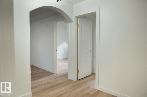 Interior hallway featuring wood-finish flooring, an arched entryway, white paneled doors with brass hardware, and clean white walls - 183 Dechene Road, Edmonton, AB 