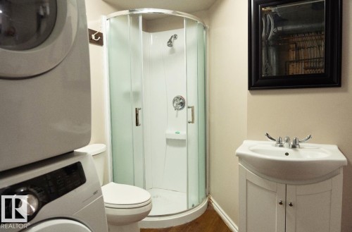 Compact bathroom featuring a corner shower enclosure, white vanity with integrated sink, and wood-finish flooring - 183 Dechene Road, Edmonton, AB 