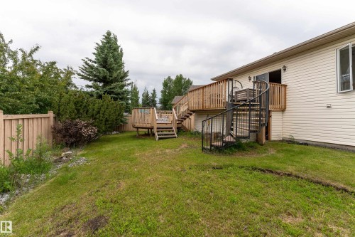 Expansive backyard featuring a multi-level wooden deck with natural wood railings, a black metal spiral staircase, and vinyl siding on the property's exterior - 183 Dechene Road, Edmonton, AB 