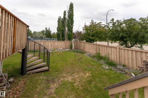 Spiral staircase with black metal railing, wooden privacy fencing, sloped lawn, and mature trees - 183 Dechene Road, Edmonton, AB 