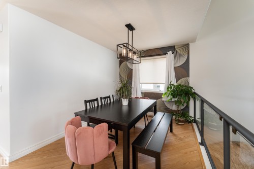 Open-concept dining area featuring hardwood flooring, a contemporary linear chandelier, and a window with roller shade - 183 Dechene Road, Edmonton, AB 