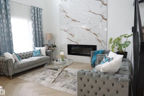 Herringbone wood-finish flooring complements a feature wall with large format stone-look tile and an integrated linear fireplace - 17703 74 Street, Edmonton, AB 