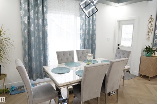 Dining area with herringbone wood-finish flooring, a white marble-look table, and a modern geometric pendant light fixture - 17703 74 Street, Edmonton, AB 