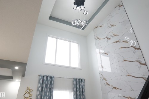 Soaring ceiling with a contemporary chandelier, a prominent marble-look accent wall, and recessed lighting - 17703 74 Street, Edmonton, AB 