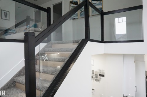 Modern staircase featuring a glass and dark-stained wood railing, carpeted treads with integrated lighting, and white risers - 17703 74 Street, Edmonton, AB 