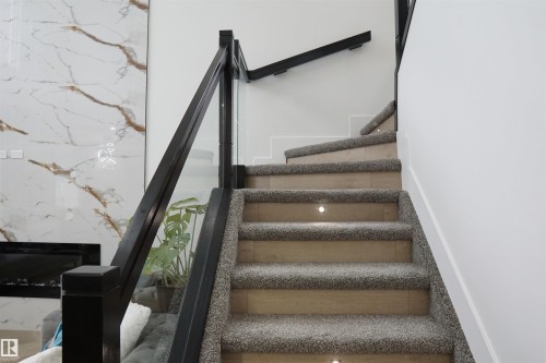 Staircase with plush carpet treads, recessed lighting, and a contemporary railing featuring dark wood and clear panels - 17703 74 Street, Edmonton, AB 