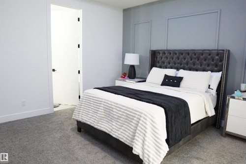 Carpeted room featuring a tufted upholstered headboard, a white interior door with black hardware, white baseboards, and a paneled accent wall - 17703 74 Street, Edmonton, AB 