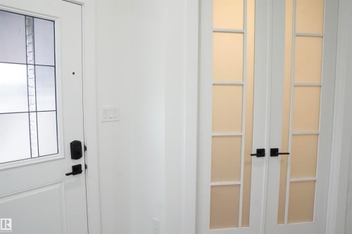 Entryway featuring a white paneled door with decorative glass inserts and matte black hardware, complemented by white interior walls and a pair of white French doors with frosted glass panels - 17703 74 Street, Edmonton, AB 