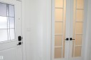 Entryway featuring a white paneled door with decorative glass inserts and matte black hardware, complemented by white interior walls and a pair of white French doors with frosted glass panels - 17703 74 Street, Edmonton, AB 