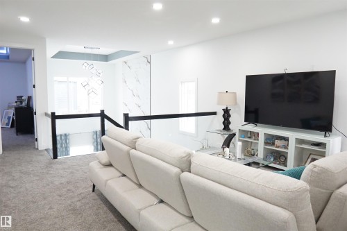 Open concept living area featuring recessed lighting, a contemporary chandelier, a white accent wall with a marble-effect panel, and modern black and glass railings - 17703 74 Street, Edmonton, AB 