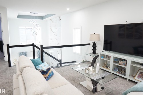 Open-concept living space featuring a modern glass railing, high ceilings, recessed lighting, and a prominent decorative light fixture - 17703 74 Street, Edmonton, AB 