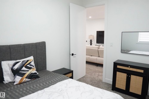 Contemporary bedroom featuring light gray walls, dark gray carpet, a solid core door with matte black hardware, and a separate living area visible through the doorway - 17703 74 Street, Edmonton, AB 