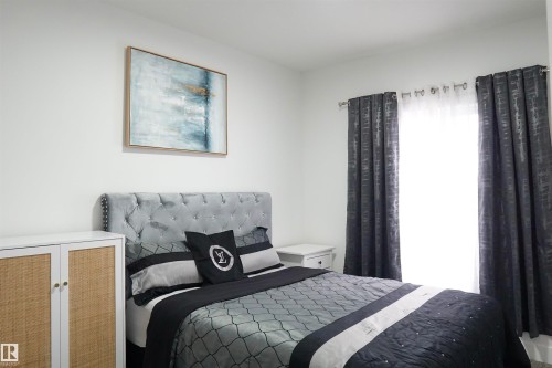 Bedroom featuring a tufted upholstered headboard, white walls, and a window dressed with dark patterned curtains and sheer panels - 17703 74 Street, Edmonton, AB 