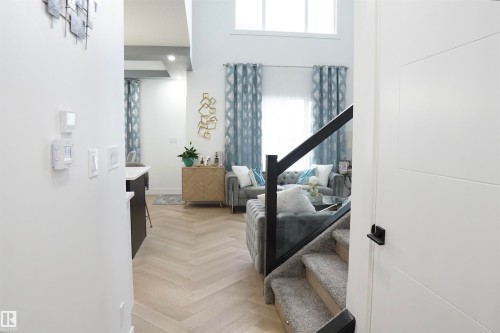 Modern interior featuring light wood-finish herringbone flooring, a contemporary staircase with glass railing, and a tall vaulted ceiling with upper windows - 17703 74 Street, Edmonton, AB 