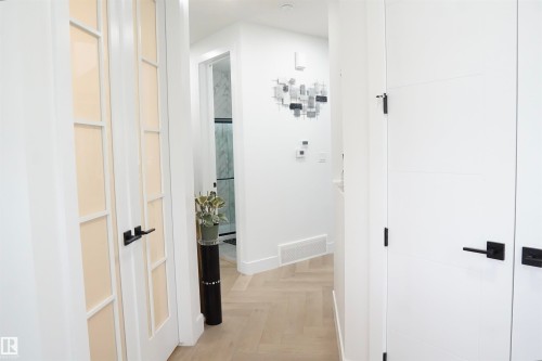 Hallway featuring wood-finish flooring in a herringbone pattern, white interior doors with black hardware, and a framed glass door - 17703 74 Street, Edmonton, AB 