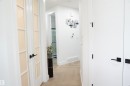 Hallway featuring wood-finish flooring in a herringbone pattern, white interior doors with black hardware, and a framed glass door - 17703 74 Street, Edmonton, AB 