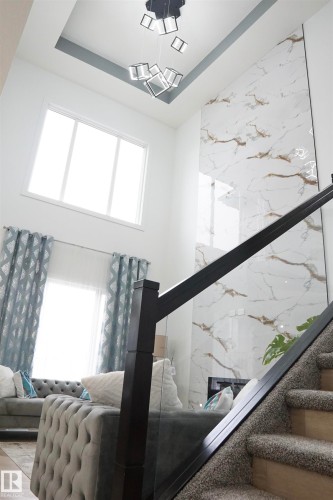 Two-story living area featuring a prominent floor-to-ceiling accent wall with a marble-effect finish, a contemporary chandelier, and high windows - 17703 74 Street, Edmonton, AB 