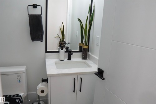 Modern bathroom featuring a white vanity with a rectangular undermount sink, a light-toned countertop, and a black framed mirror - 17703 74 Street, Edmonton, AB 