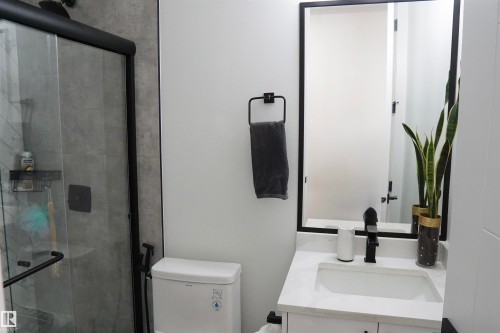 Modern bathroom featuring a glass shower enclosure with matte black framing, a wall-mounted vanity with a white countertop and integrated sink, a rectangular mirror with a black frame, and a white toilet - 17703 74 Street, Edmonton, AB 