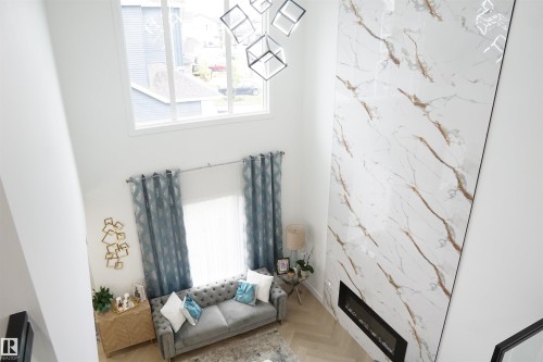 Living area featuring a floor-to-ceiling fireplace with white and gold veined surfacing, a built-in linear electric fireplace, and a high ceiling - 17703 74 Street, Edmonton, AB 
