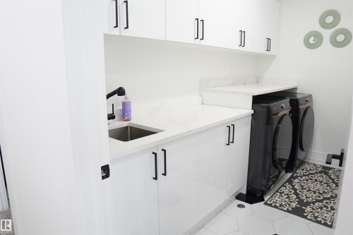 Bright utility space featuring white cabinetry with matte black hardware, a stainless steel sink with a matte black faucet, and white countertops - 17703 74 Street, Edmonton, AB 
