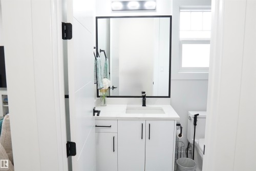 Modern bathroom featuring a white vanity with integrated sink, black-framed mirror, and a window for natural light - 17703 74 Street, Edmonton, AB 