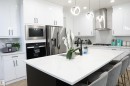 Contemporary kitchen featuring white high-gloss cabinetry, stainless steel appliances, a center island with seating, pendant lighting, and a tile backsplash - 17703 74 Street, Edmonton, AB 