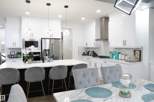 Modern kitchen featuring a large central island with seating, white high-gloss cabinetry, stainless steel appliances, and recessed lighting - 17703 74 Street, Edmonton, AB 