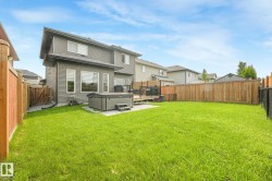 Expansive backyard featuring a manicured lawn, a built-in hot tub on a concrete pad, a wooden privacy fence, and a multi-level deck with dark railings - 
