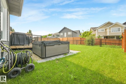 Spacious backyard featuring a hot tub on a paver patio, a wooden deck, and a manicured lawn, enclosed by both wood and chain-link fencing - 556 Merlin Landing Landing, Edmonton, AB 