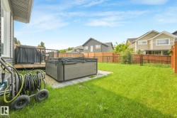 Spacious backyard featuring a hot tub on a paver patio, a wooden deck, and a manicured lawn, enclosed by both wood and chain-link fencing - 