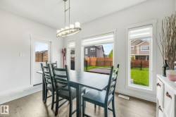 Bright dining area featuring wood-finish flooring, a contemporary linear chandelier, multiple windows with blinds, and a rear exterior door - 