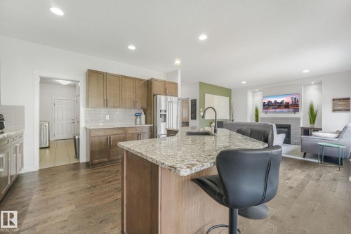 Open-concept kitchen and living area featuring wood-finish flooring, recessed lighting, and a granite-topped kitchen island with an undermount sink and matte black faucet - 556 Merlin Landing Landing, Edmonton, AB 