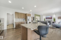 Open-concept kitchen and living area featuring wood-finish flooring, recessed lighting, and a granite-topped kitchen island with an undermount sink and matte black faucet - 