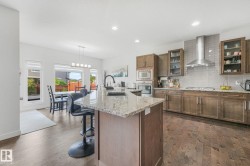 Kitchen featuring a granite countertop island with a built-in sink, wood-finish cabinetry, stainless steel appliances, a tile backsplash, and recessed lighting - 