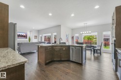 Open-concept living space featuring wood-finish flooring, recessed lighting, and a kitchen island with stone countertops and a built-in stainless steel dishwasher - 