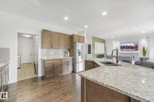 Kitchen featuring an extended island with a built-in sink, stainless steel appliances, wood-finish cabinetry, and a subway tile backsplash - 556 Merlin Landing Landing, Edmonton, AB 