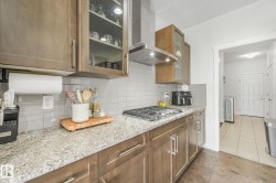 Kitchen featuring granite countertops, wood cabinetry, a tile backsplash, and a stainless steel range hood - 