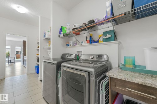 Dedicated laundry space featuring a side-by-side washer and dryer, tile flooring, and integrated wire shelving for storage - 556 Merlin Landing Landing, Edmonton, AB 