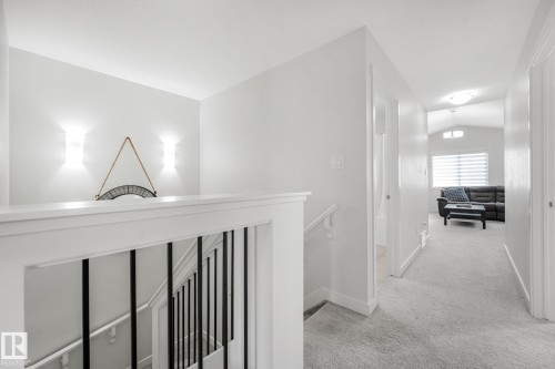 Upper-level hallway featuring light gray carpeting, white walls, and a white banister with black iron balusters - 556 Merlin Landing Landing, Edmonton, AB 
