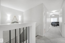 Upper-level hallway featuring light gray carpeting, white walls, and a white banister with black iron balusters - 