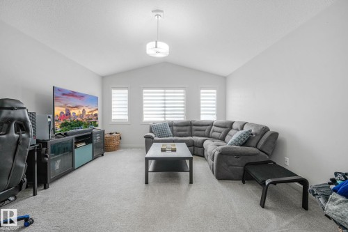 Vaulted ceiling living space featuring light gray carpeting, neutral wall tones, multiple windows with horizontal blinds, and a suspended ceiling fixture - 556 Merlin Landing Landing, Edmonton, AB 
