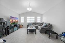 Vaulted ceiling living space featuring light gray carpeting, neutral wall tones, multiple windows with horizontal blinds, and a suspended ceiling fixture - 