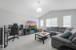 Spacious living area featuring light gray carpeting, vaulted ceilings, a contemporary ceiling light fixture, and multiple windows with horizontal blinds - 