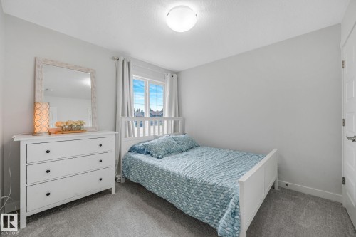 Bedroom featuring a window with exterior scenery, light gray walls, textured gray carpeting, a single ceiling light fixture, and white baseboards - 556 Merlin Landing Landing, Edmonton, AB 