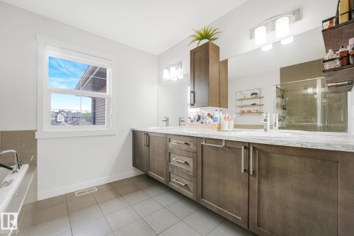 Bathroom featuring a double vanity with light-toned countertops, integrated sinks, and dark wood-finish cabinetry - 556 Merlin Landing Landing, Edmonton, AB 