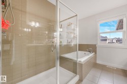 Bathroom featuring a glass-enclosed shower, a built-in soaking tub, beige ceramic tile flooring, a window with white trim, and a tiled tub surround - 