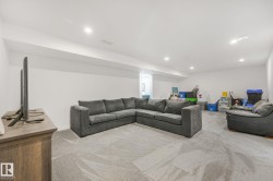 Spacious lower-level room featuring light gray carpeting, recessed ceiling lighting, and crisp white walls - 